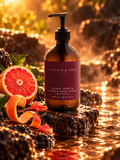 Ruby Vista Hand & Body Wash beside a cut pink grapefruit in a warm candlelit setting.